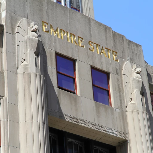 Close-up of the Empire State Building's lower facade, showing detailed Art Deco gold lettering and sculpted eagles above vertical columns, exuding luxury and power.